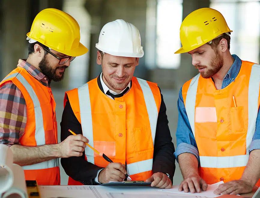 Équipe de travailleurs en casque et dossard, souriants, autour d'un plan